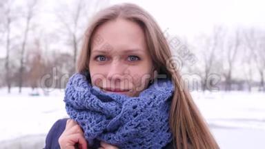 穿着<strong>蓝色</strong>针织围巾的漂亮蓝眼睛女人在冬天的城市公园里，她看着摄像机，<strong>纠正</strong>着她的长尾巴